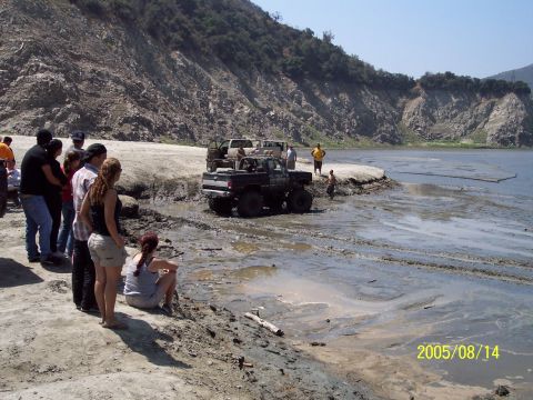1985 Ford Bronco - Off-road vehicles stuck in mud by a lake, with onlookers observing the scene. Date stamp: 2005/08/14.