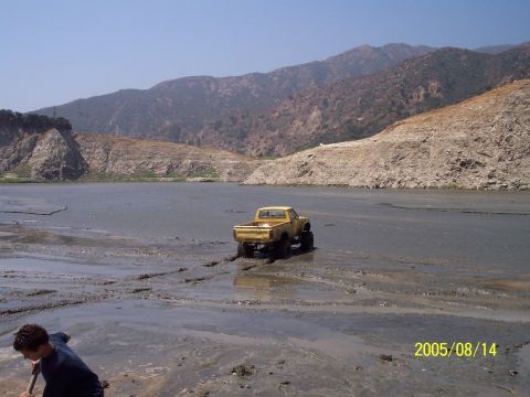 1985 Ford Bronco - Yellow pickup truck navigates muddy terrain with mountains in the distance. Date stamp: 2005/08/14.