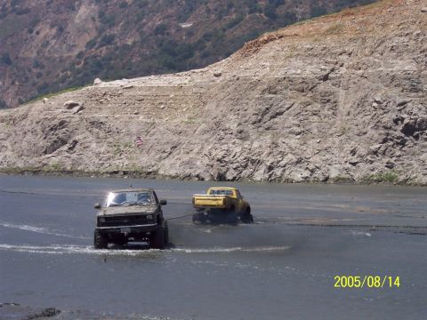 1985 Ford Bronco - Two trucks are stuck in the mud, with one attempting to pull the other out.