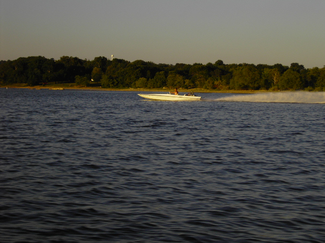 White speed boat moving across dark water, trees and sky in background