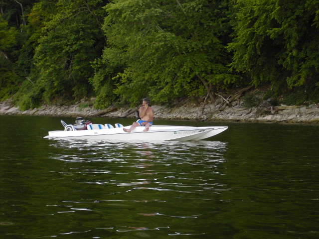 Long white flat-deck race-style speedboat with open engine on a wooded lake