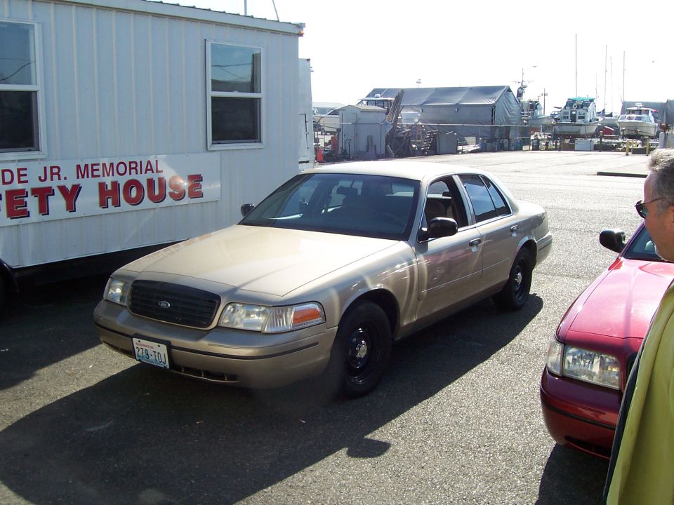 Gold 2003 Ford Crown Victoria parked next to a red car, with a white building behind it