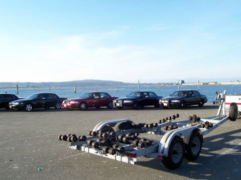2003 Ford Crown Victoria - Several Ford Crown Victorias are lined up next to a boat trailer with a waterfront view.
