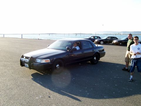 2003 Ford Crown Victoria - A group of people stand near a fleet of Ford Crown Victoria police cars parked along a waterfront promenade.