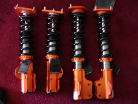 1989 Mazda MX-6 - Set of four orange coilover suspension assemblies, likely aftermarket performance parts, displayed on a red surface.