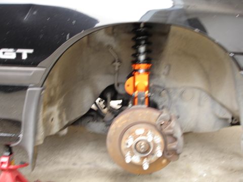 1989 Mazda MX-6 - Close-up view of the front wheel well, the brake system and an orange coilover suspension component.
