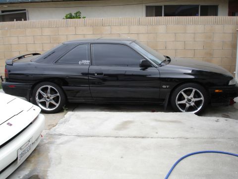 1989 Mazda MX-6 - A black coupe with tinted windows and a rear spoiler is parked on a concrete driveway.