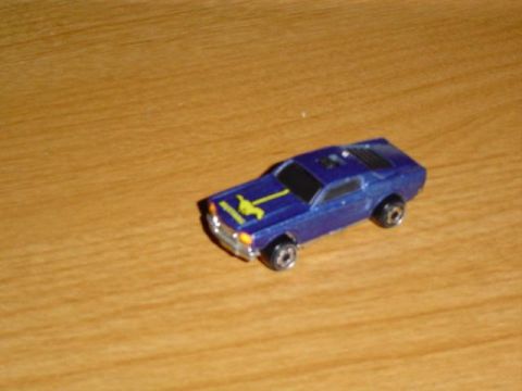 1979 Ford Bronco - A blue toy car with a yellow stripe is pictured on a wooden surface.