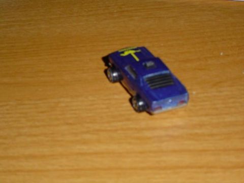 1979 Ford Bronco - A small blue toy car with a yellow stripe is positioned on a wooden surface.
