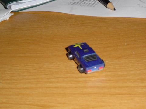 1979 Ford Bronco - A small blue toy car with a yellow stripe is viewed from the rear on a wooden surface.