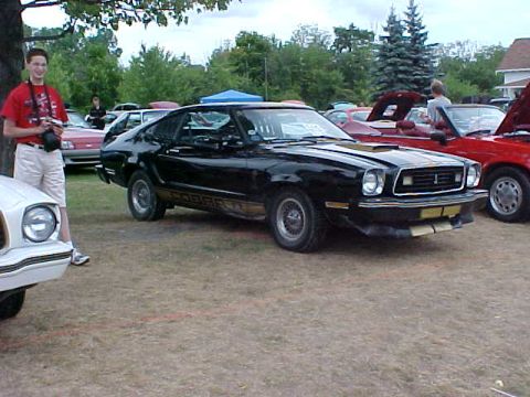 1978 Ford Mustang II - A black 1978 Ford Mustang II is parked on a grassy lot, with other vehicles visible in the background.