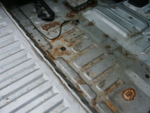 1982 Ford Bronco - Interior floor pan shows significant rust and wear. Wiring and seat belt anchor points are visible.