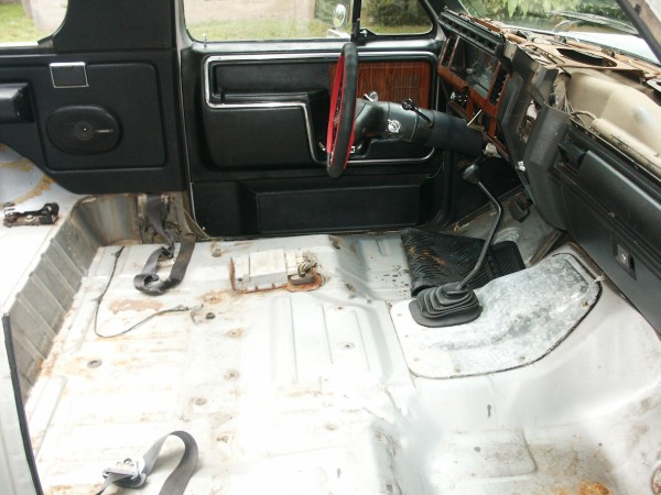 Interior of a white truck with exposed metal floor, black door panel, and red steering wheel
