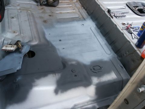1982 Ford Bronco - The interior floor of a vehicle is shown, with some areas prepped for a spray-in liner and tools laid out.