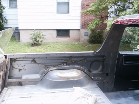 1982 Ford Bronco - The interior of a truck bed is shown, with visible rust and dirt on the metal surfaces.