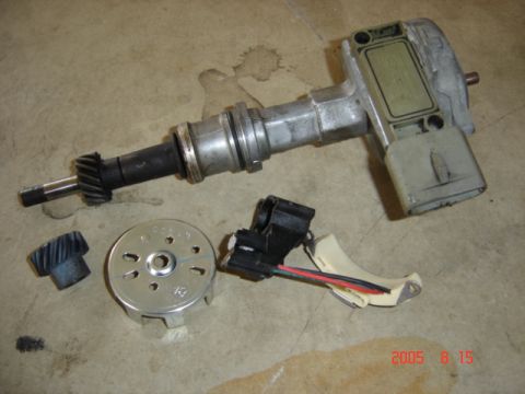 1990 Ford Bronco - A disassembled distributor laid out on a concrete floor, with the aluminum housing and drive gear at top and its ignition control module bo…