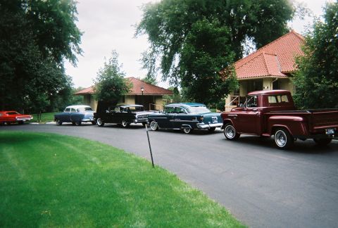 1972 Ford Ranchero - A line of vintage cars, including a maroon pickup and a blue sedan, are parked in front of houses.