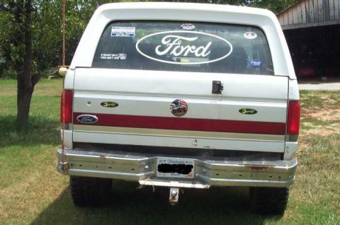 1988 Ford Bronco - The rear of a Ford Bronco, showing its distinctive body style and a large Ford oval decal on the back window.