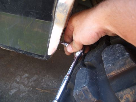 1988 Ford Bronco - A hand tightens a screw on the fender trim of a vehicle, with a large tire visible.