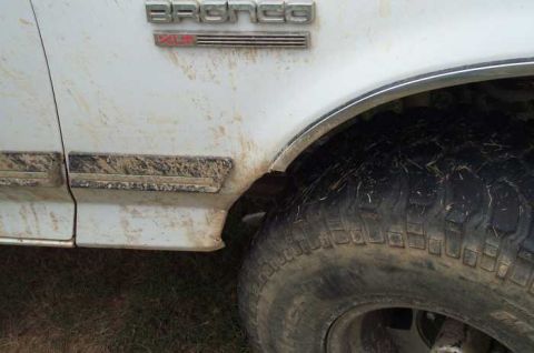 1988 Ford Bronco - Mud-splattered 1988 Ford Bronco shows its side profile and 'Bronco' badging.