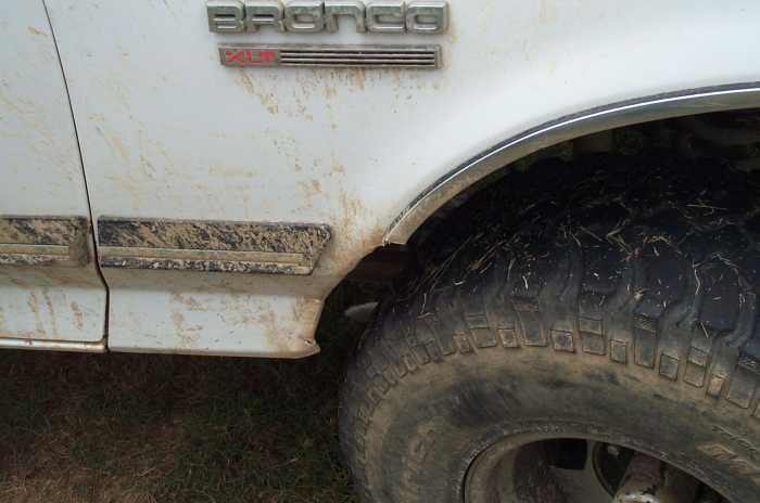 Mud-splattered white Ford Bronco XLT fender badge and mud tire in the wheel well
