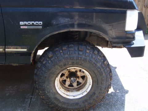 1988 Ford Bronco - Close-up of a black Ford Bronco's front fender and large off-road tire, with "Bronco" badging visible.