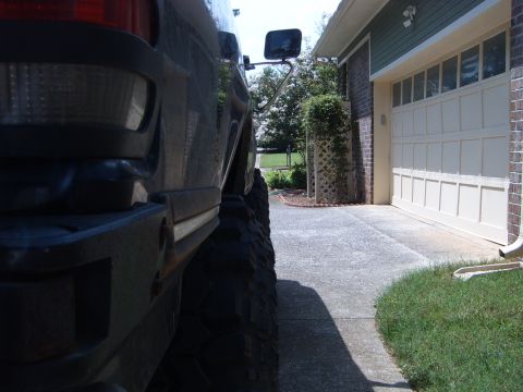 1988 Ford Bronco - Close-up view of the rear fender and tire of a dark SUV, seen from the side, parked on a driveway next to a garage.