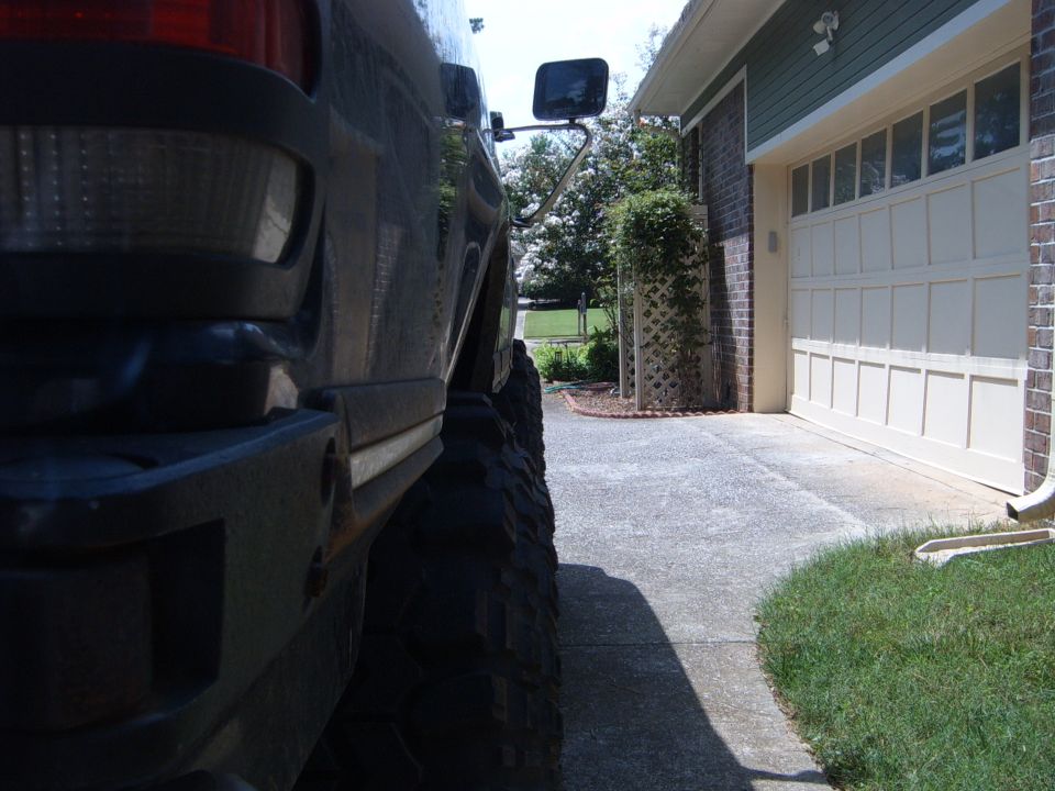 Rear fender and large tire of a dark SUV parked next to a garage