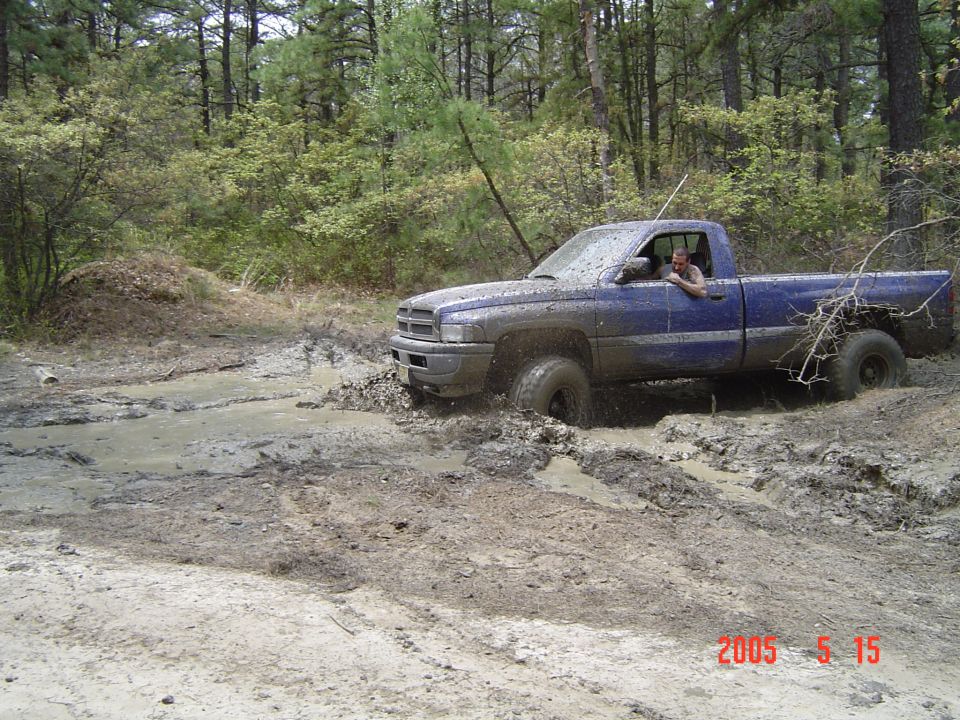 Blue 1995 Dodge 1500 pickup truck with a single cab stuck in a muddy trail, front 3/4 view