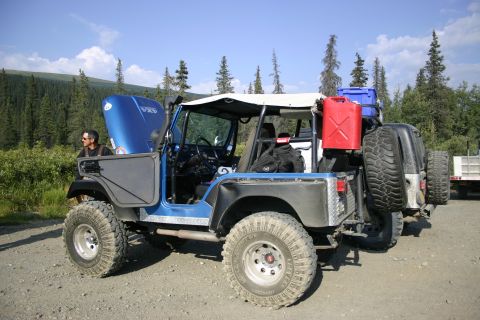 2003 Jeep TJ - Modified blue Jeep CJ parked on a dirt road with trees and sky in the background.