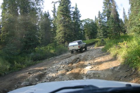 2003 Jeep TJ - A pickup truck navigates a challenging off-road path through a forest.