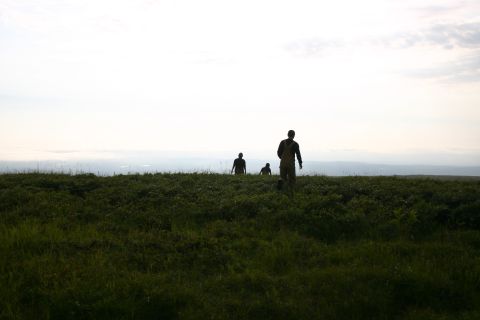 2003 Jeep TJ - Three figures traverse a vast, green landscape under an overcast sky.