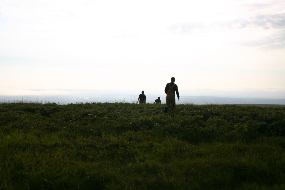 Three people walk across a grassy hill under a hazy sky
