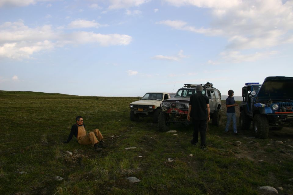Three modified off-road Jeeps parked on a grassy hill under a cloudy sky