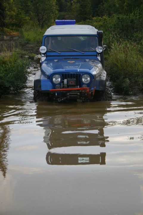 2003 Jeep TJ - A blue Jeep navigates a water obstacle, its reflection distorted in the murky water.