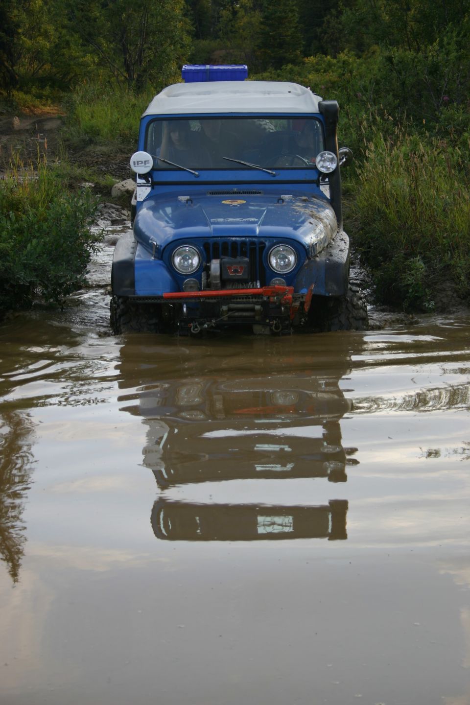 Blue Jeep with a light bar on top driving through a muddy water crossing