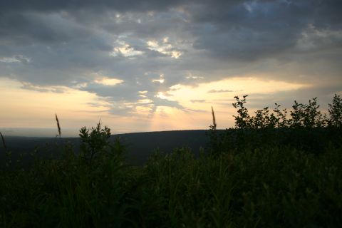2003 Jeep TJ - Sunbeams pierce the clouds at sunset, casting light over a grassy landscape.