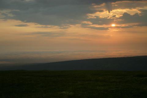 2003 Jeep TJ - A sunset casts a warm glow over a vast expanse of clouds, with a dark forest visible below the horizon.