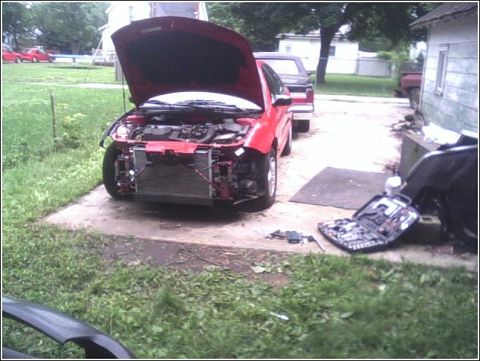 2005 Chevrolet Cavalier - A red car sits outside with its hood up and front bumper removed, suggesting body work is in progress.