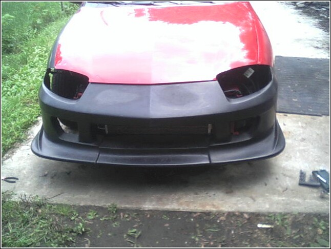 red car front end, missing headlights, with a black aftermarket bumper installed