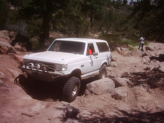 White lifted Ford Bronco with light bar parked among large rocks on a trail