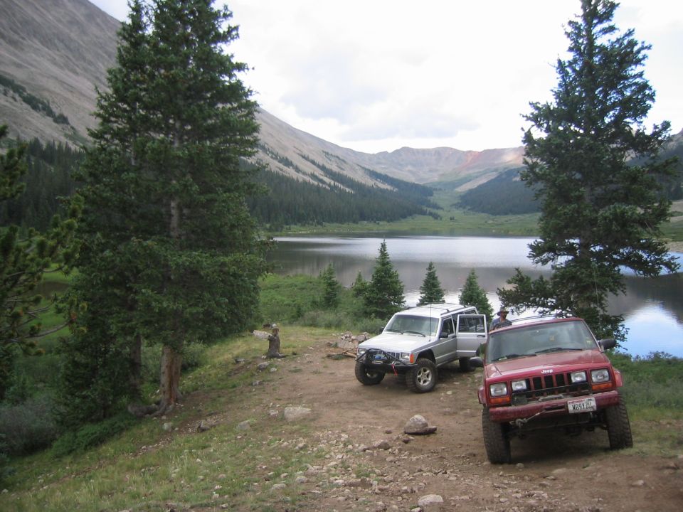1997 Jeep Cherokee and another Jeep Cherokee parked by a lake with mountains in the background