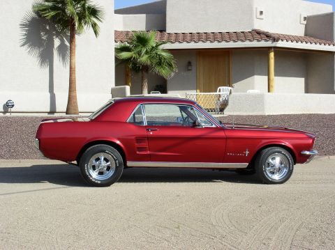 1967 Ford Mustang - Side profile of a red 1967 Ford Mustang coupe with chrome wheels parked outdoors.