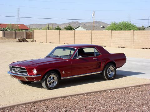 1967 Ford Mustang - A classic red 1967 Ford Mustang coupe is shown from a three-quarter front view in an outdoor setting.