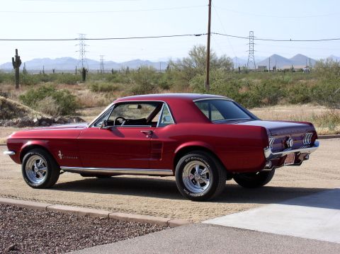 1967 Ford Mustang - A red 1967 Ford Mustang coupe is viewed from the rear three-quarter angle in a desert setting.