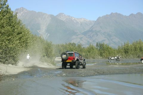 2003 Jeep TJ - Red Jeep TJ Wrangler navigates a muddy trail with mountains looming behind.