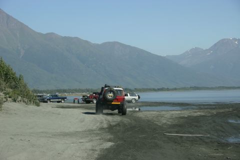 2003 Jeep TJ - Multiple vehicles are gathered near a body of water with a mountainous backdrop under a clear blue sky.