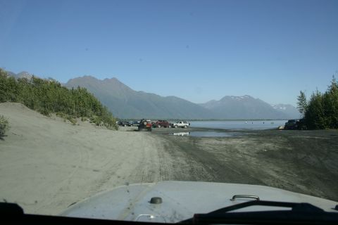 2003 Jeep TJ - Several vehicles are parked near a body of water with mountains in the background.