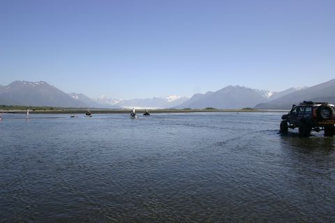 2003 Jeep TJ - A Jeep Wrangler navigates a shallow riverbed with a mountain range under a clear blue sky.