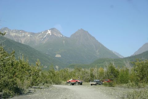 2003 Jeep TJ - Off-road vehicles are parked on a dirt road with mountains and trees in the background under a clear blue sky.